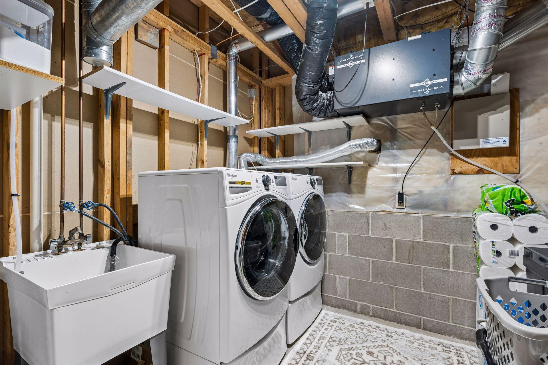 Laundry room with front-loading washer and dryer, utility sink, and exposed ceiling ductwork.