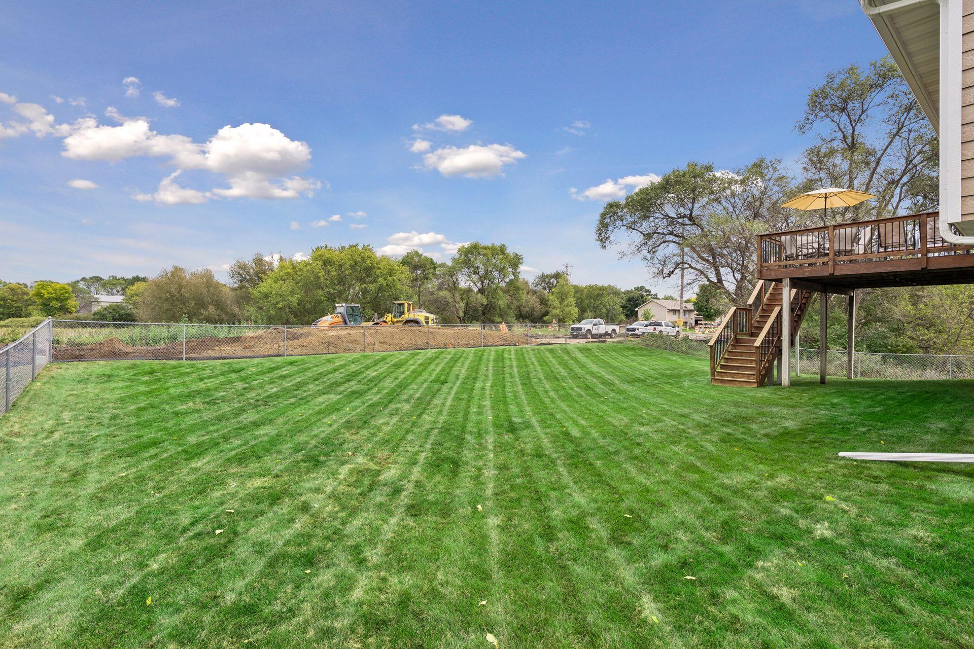 Fenced backyard with a broad striped lawn and raised wooden deck.