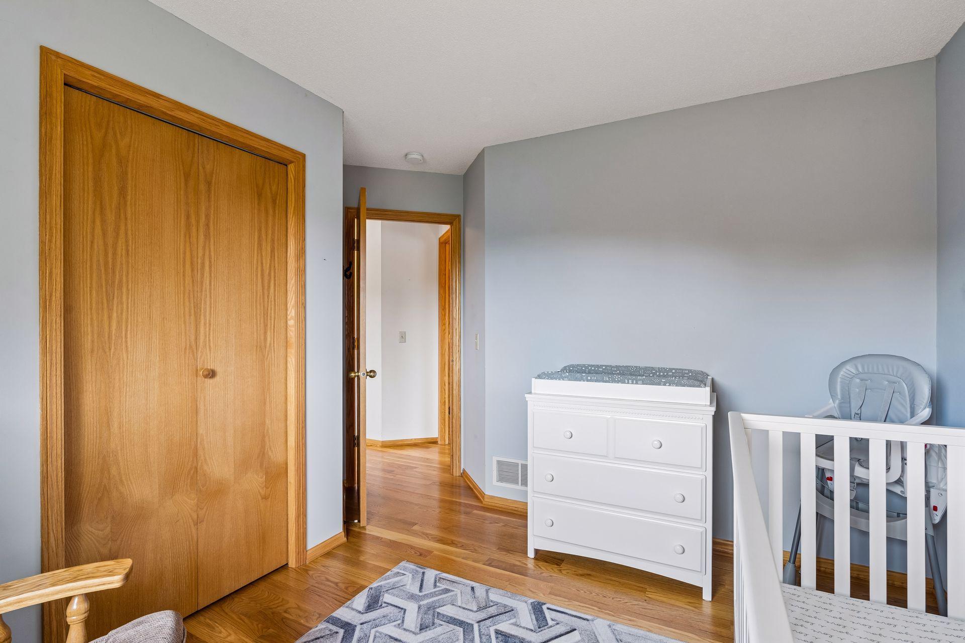 Nursery with a white crib and dresser, gray walls, and hardwood floors.