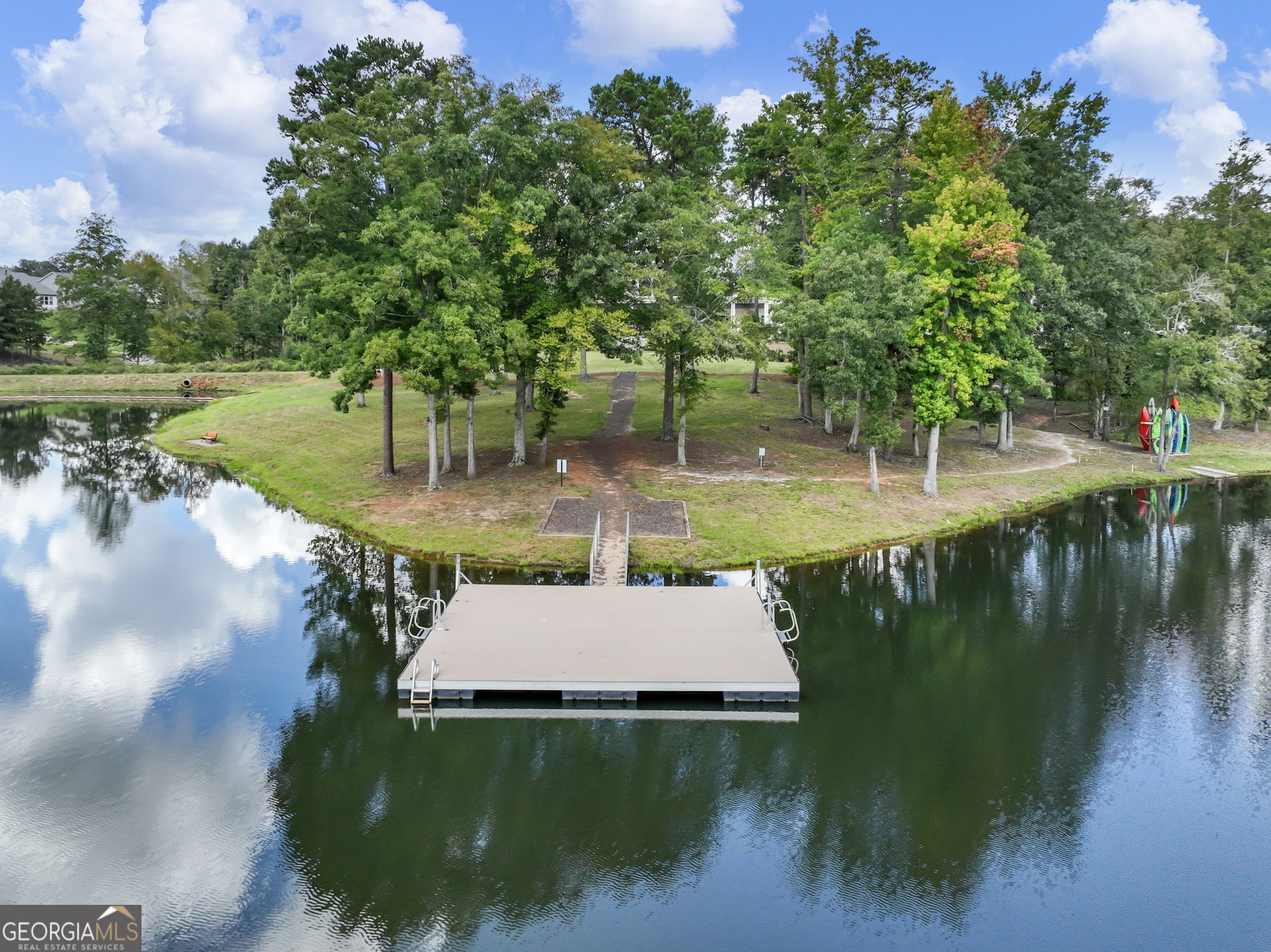 Pond with a floating dock, wooded shoreline, and colorful kayaks.