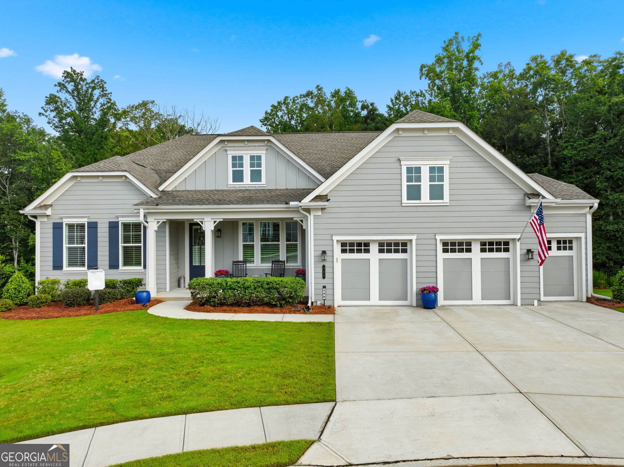 Gray two-story house with a covered porch, three garage doors, broad driveway, and American flag.
