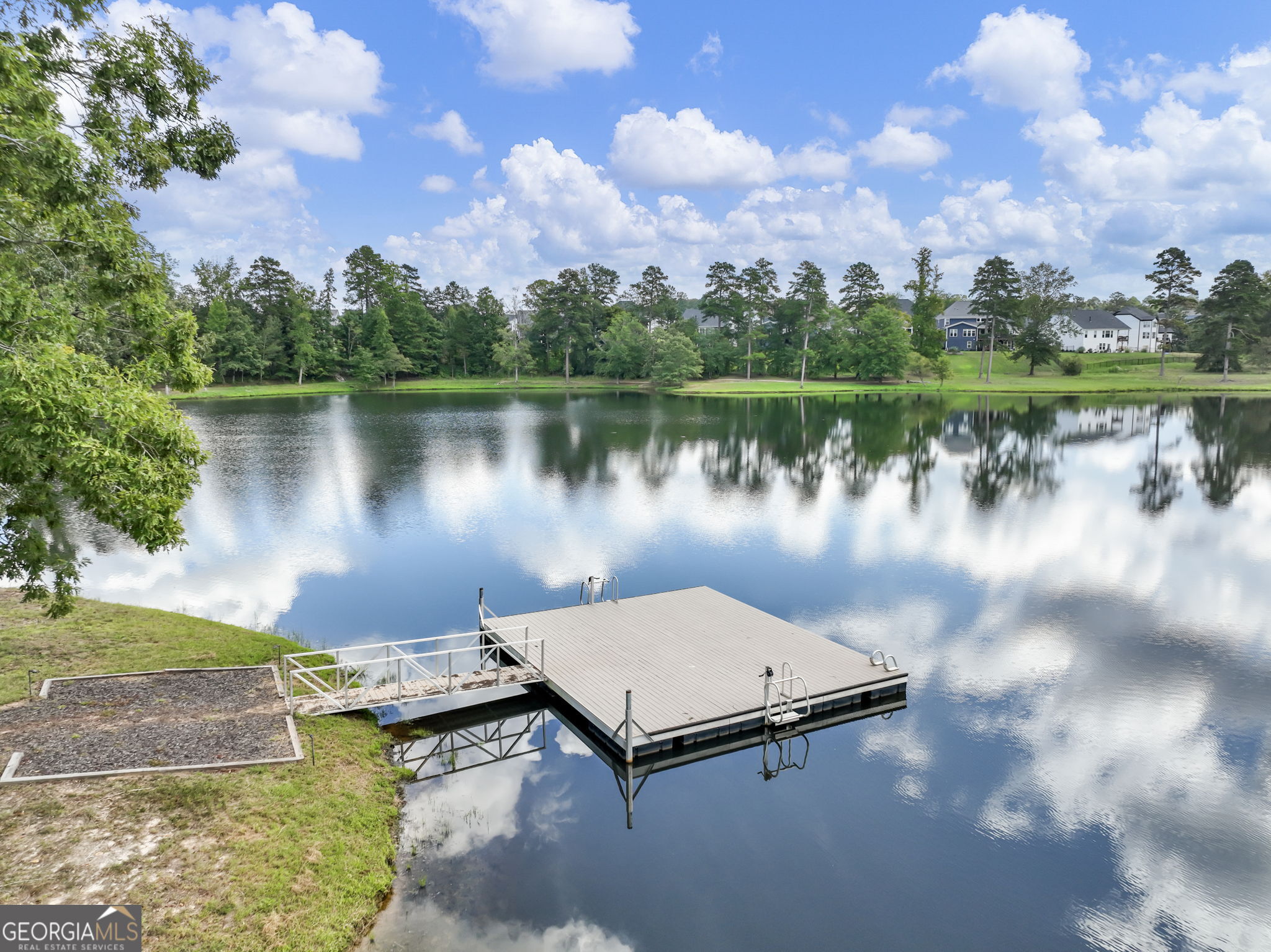 Lakefront dock with a metal access ramp, calm water, and tree-lined shore.