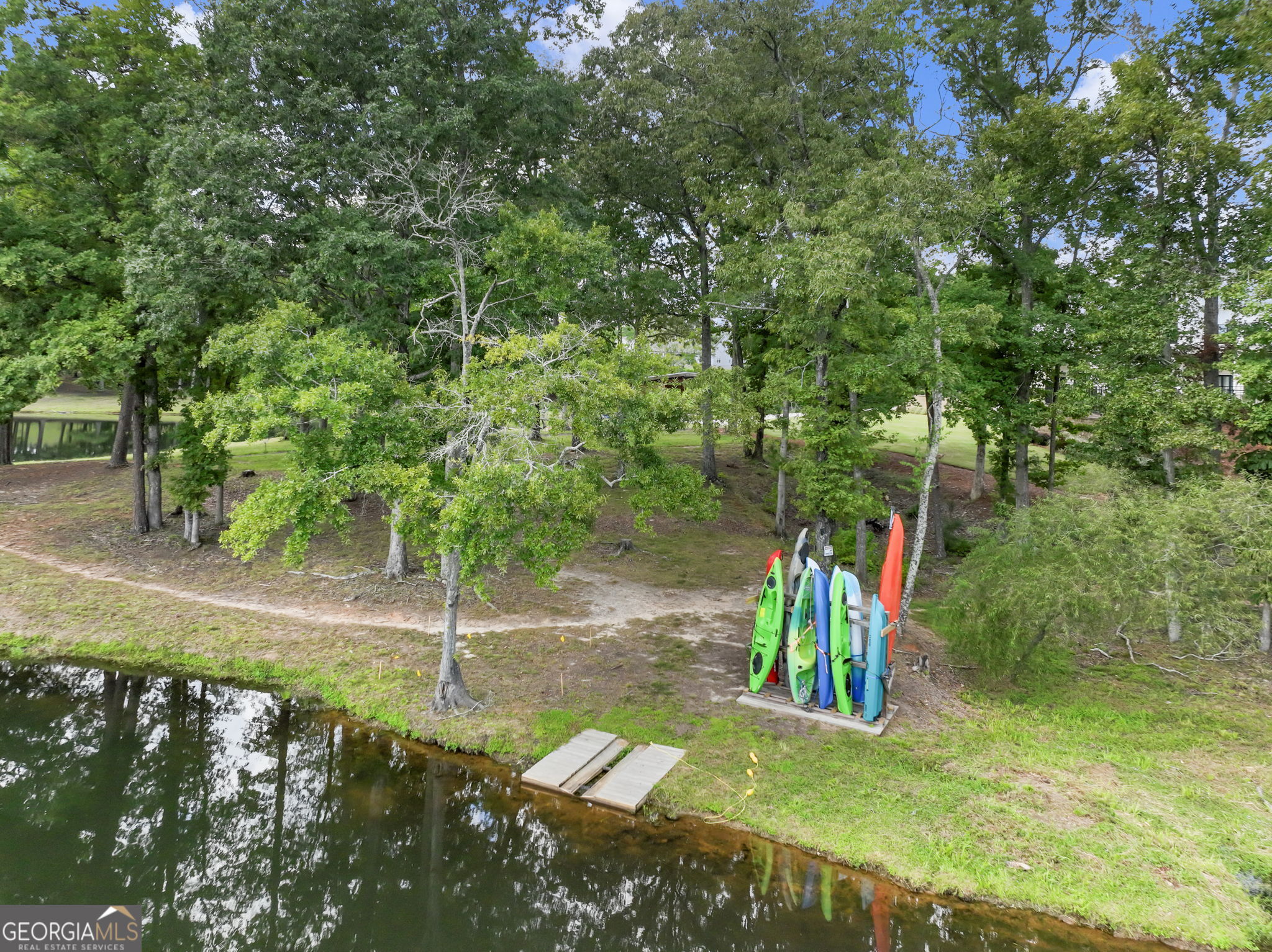 Wooded waterfront property with colorful kayaks stored beside a small dock.