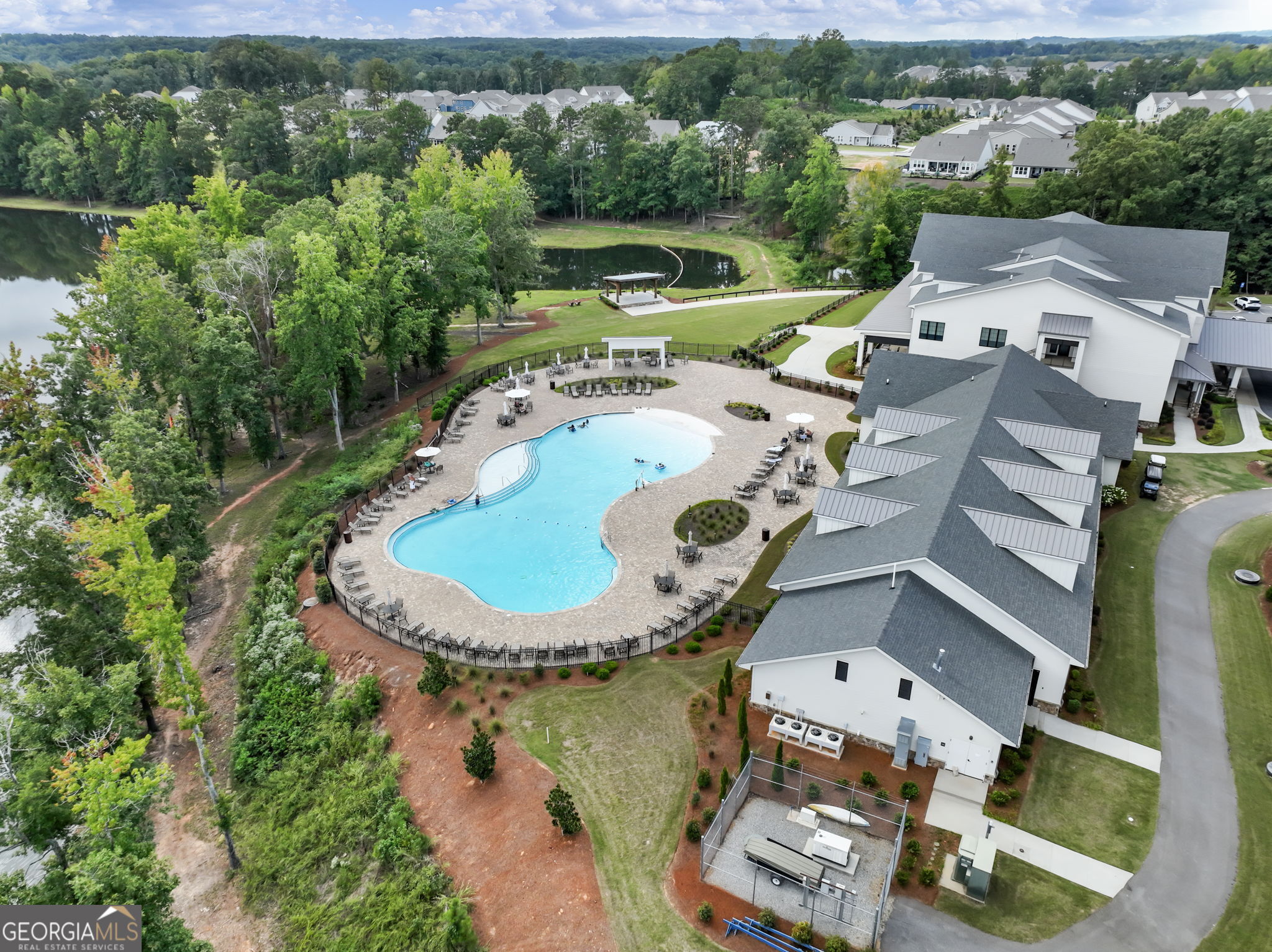 Aerial view of a community pool and clubhouse beside a wooded pond.