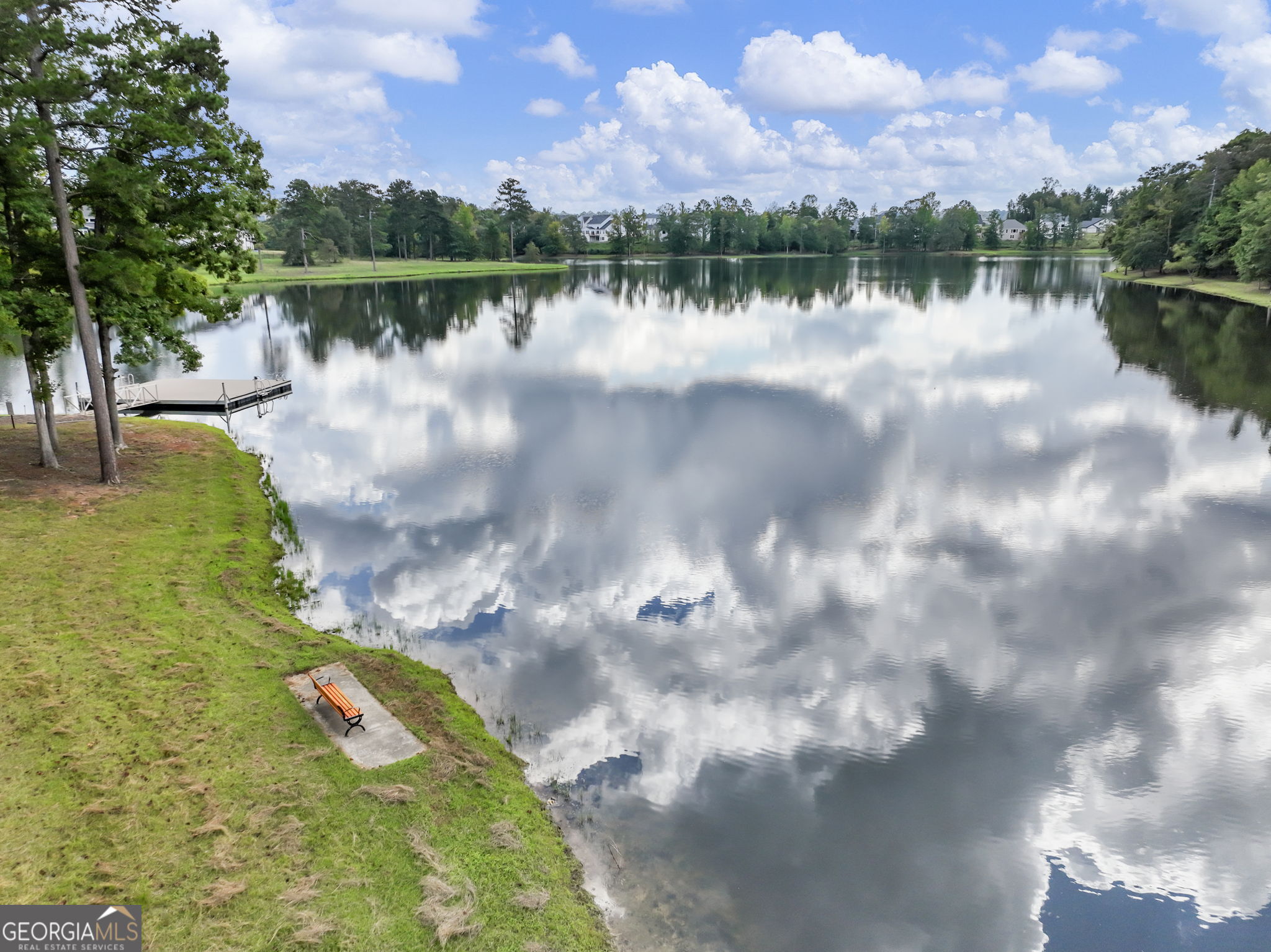 Neighborhood lake reflecting clouds, with a small dock and bench along the grassy shore.