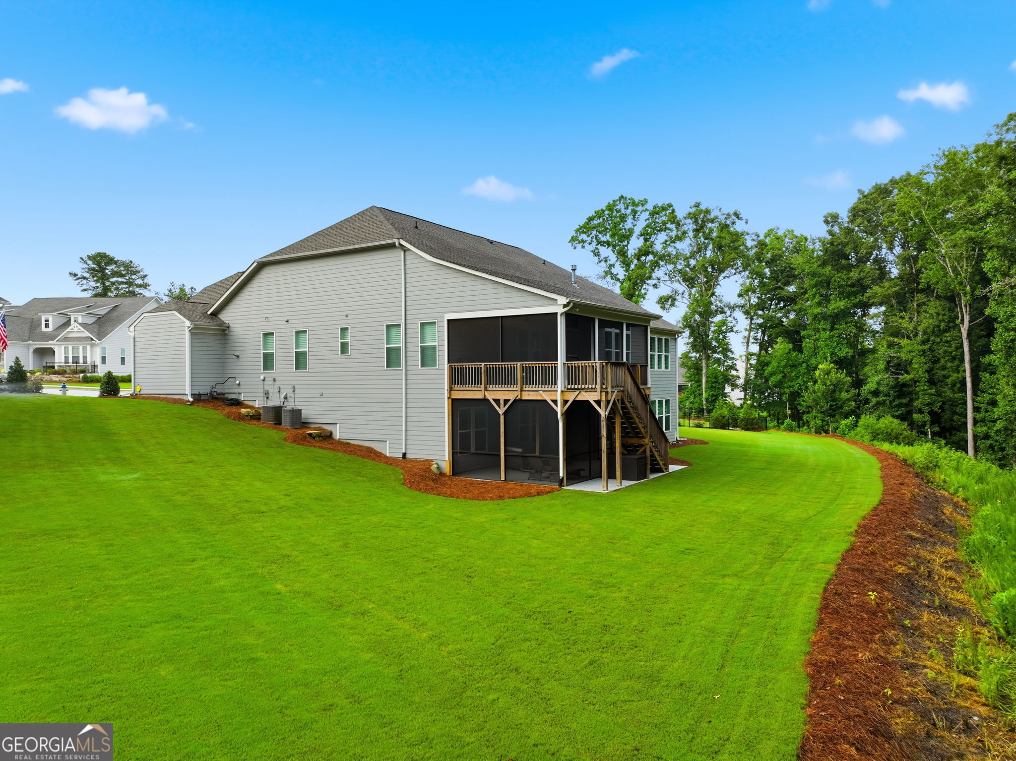 Rear of a gray two-story home with a screened deck and stairs overlooking a broad green lawn.