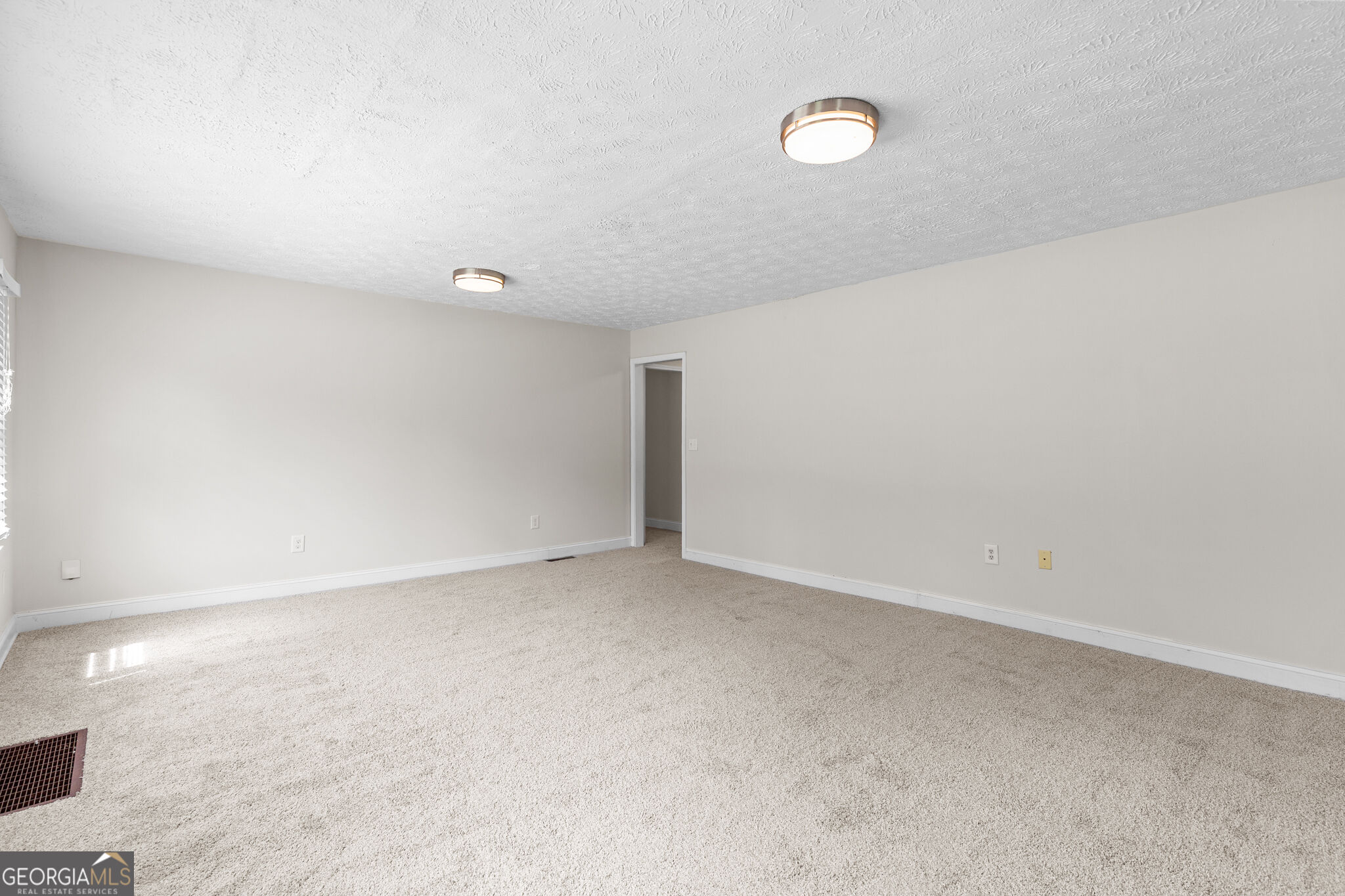 Empty carpeted room with two ceiling lights, a window, and an open doorway.