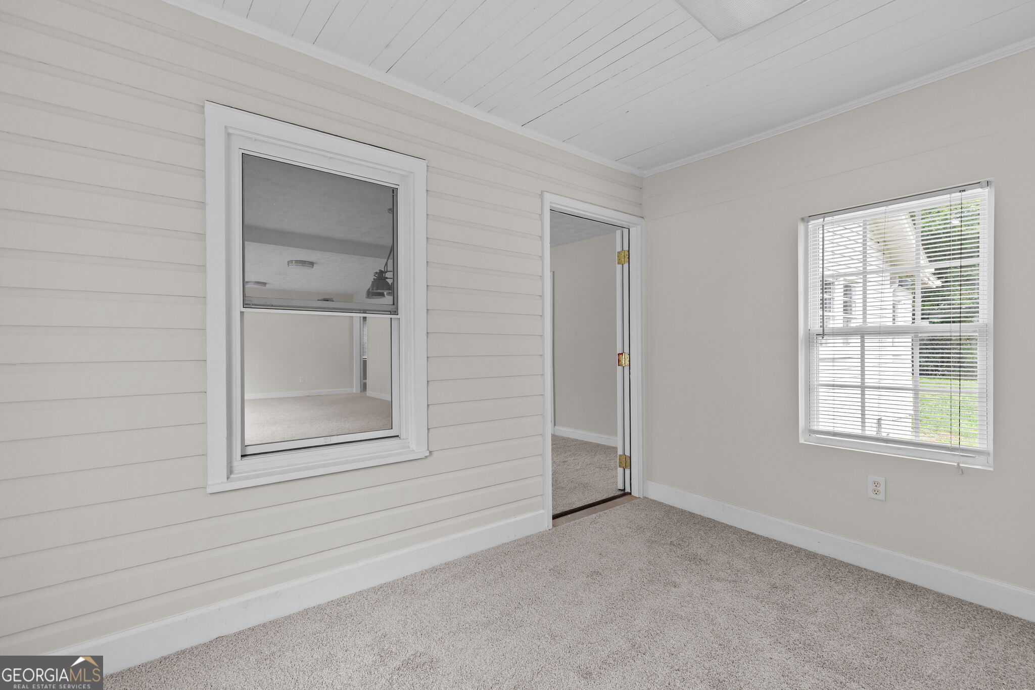 Vacant carpeted room with paneled walls, window blinds, and an open doorway.