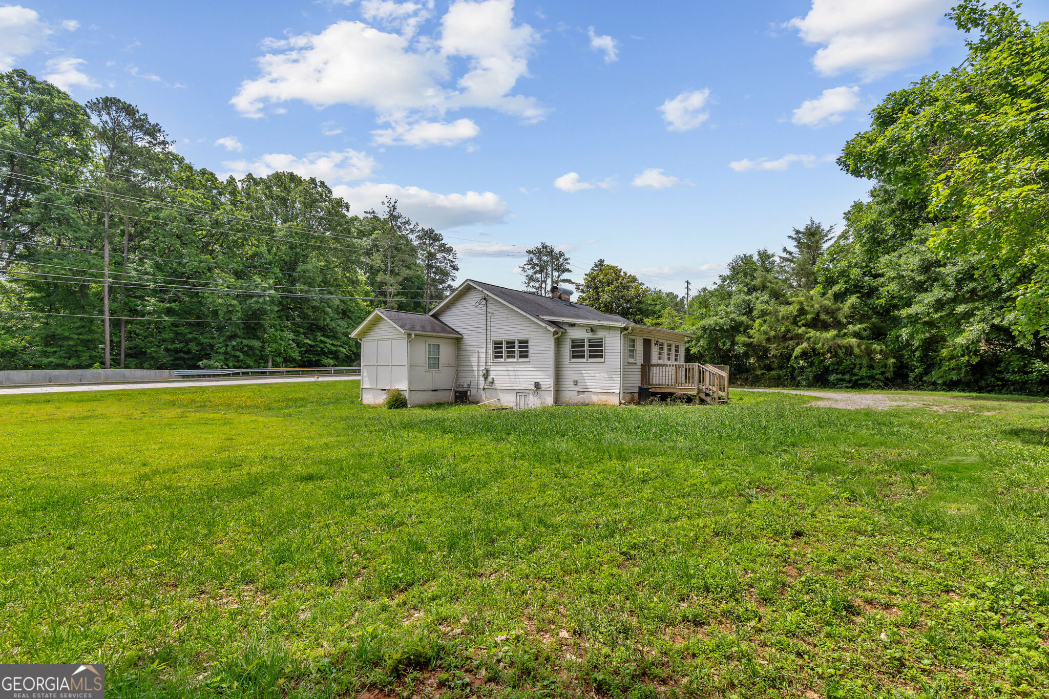 White-sided house with a raised wooden deck, broad lawn, and wooded surroundings.