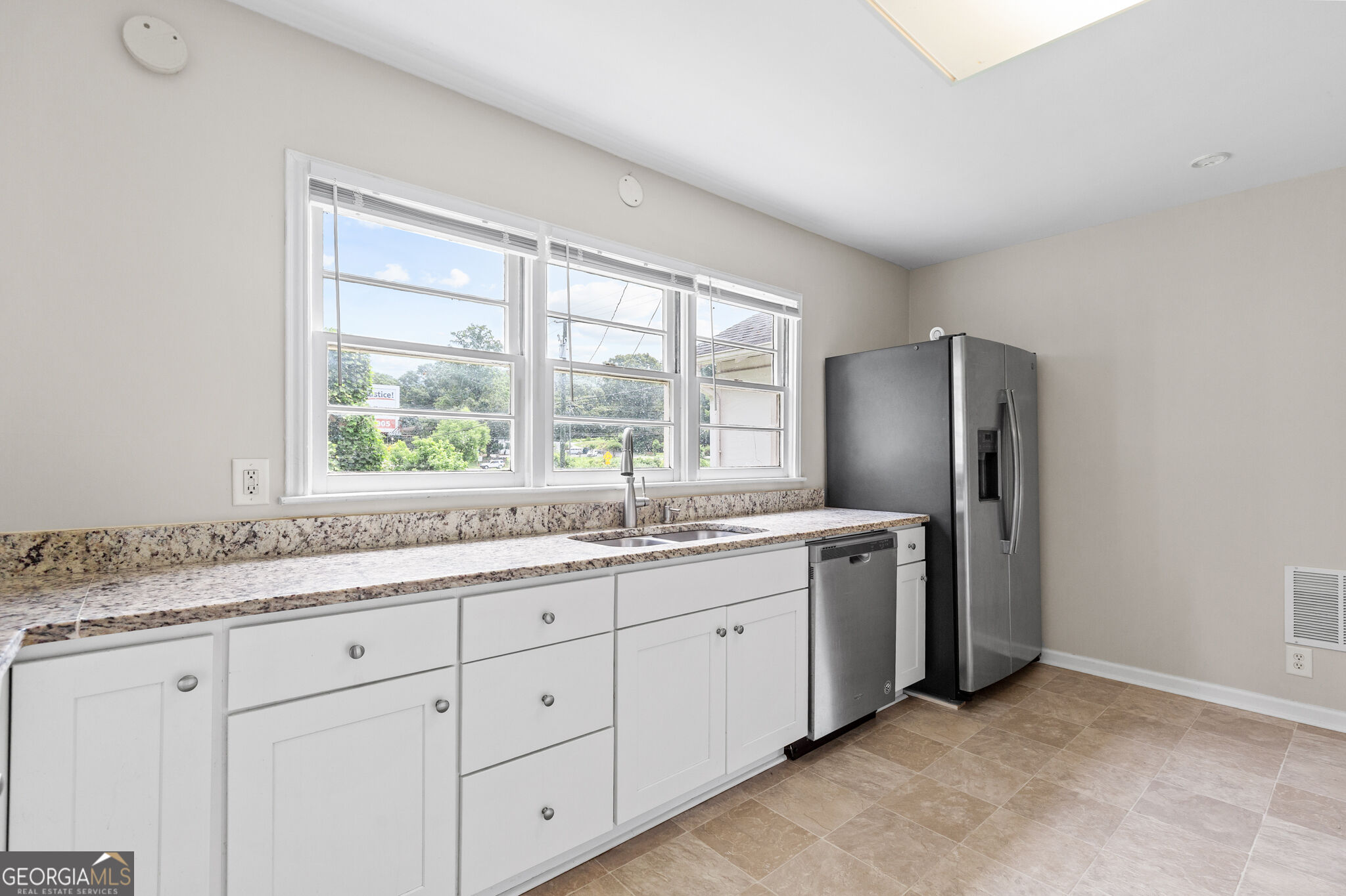 Kitchen with white cabinets, granite counters, stainless steel appliances, and large windows above the sink.