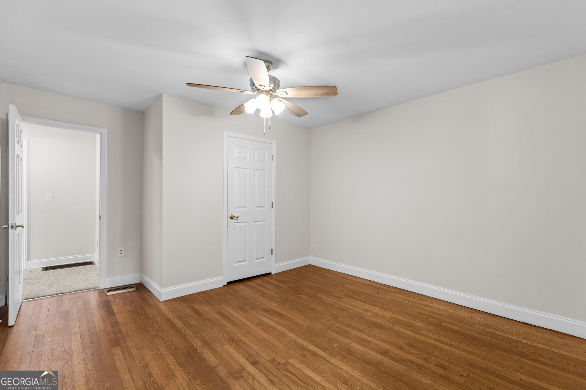 Empty room with hardwood floors, a ceiling fan, and white doors.