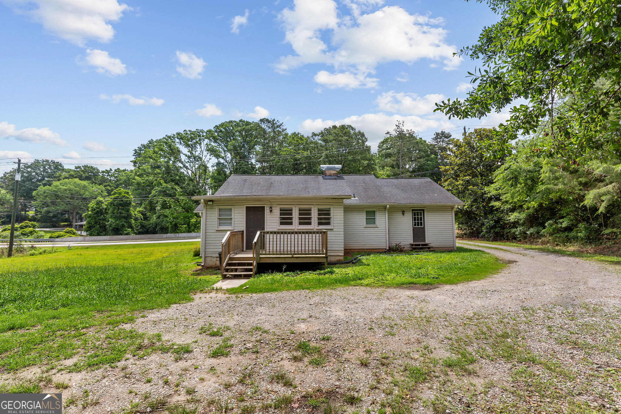Single-story house with a small wooden porch, green lawn, and broad gravel driveway.