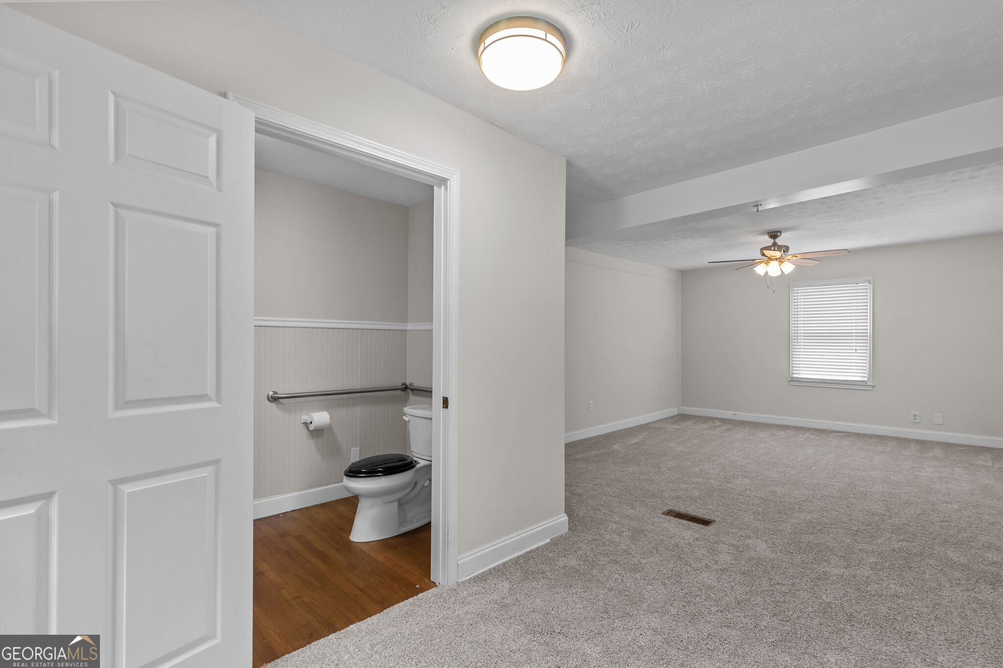 Carpeted room with a ceiling fan and window beside an adjoining bathroom.