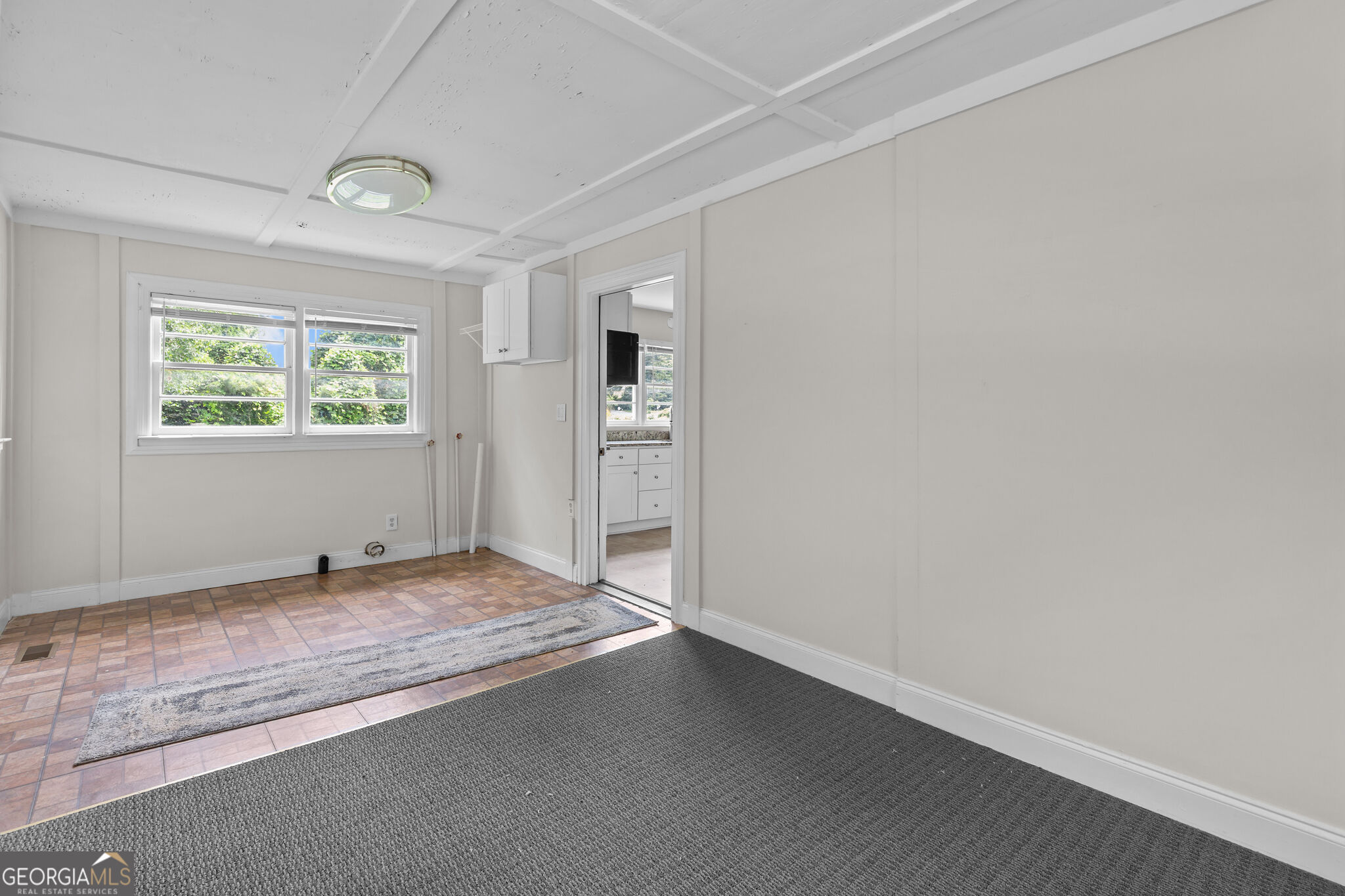 Empty room with gray carpet, tiled floor area, and a window overlooking greenery.