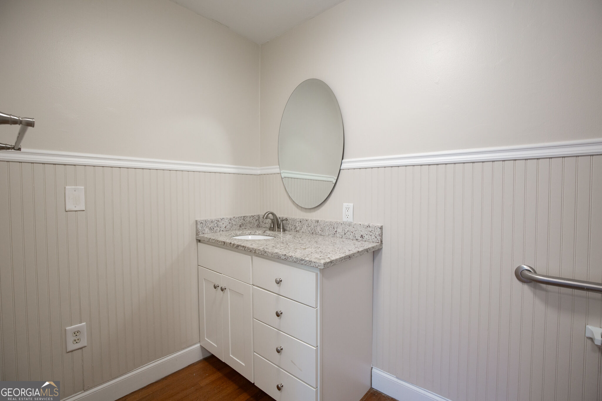 Bathroom vanity with granite countertop, oval mirror, and white beadboard wainscoting.