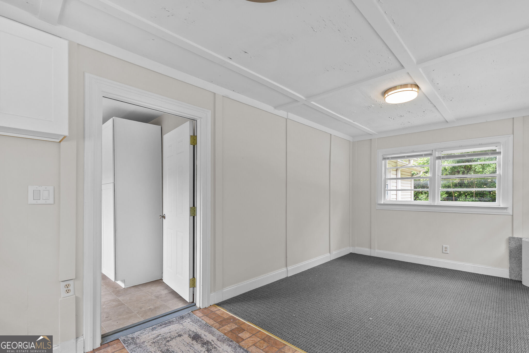 Empty carpeted room with paneled walls, a low beamed ceiling, and a window.