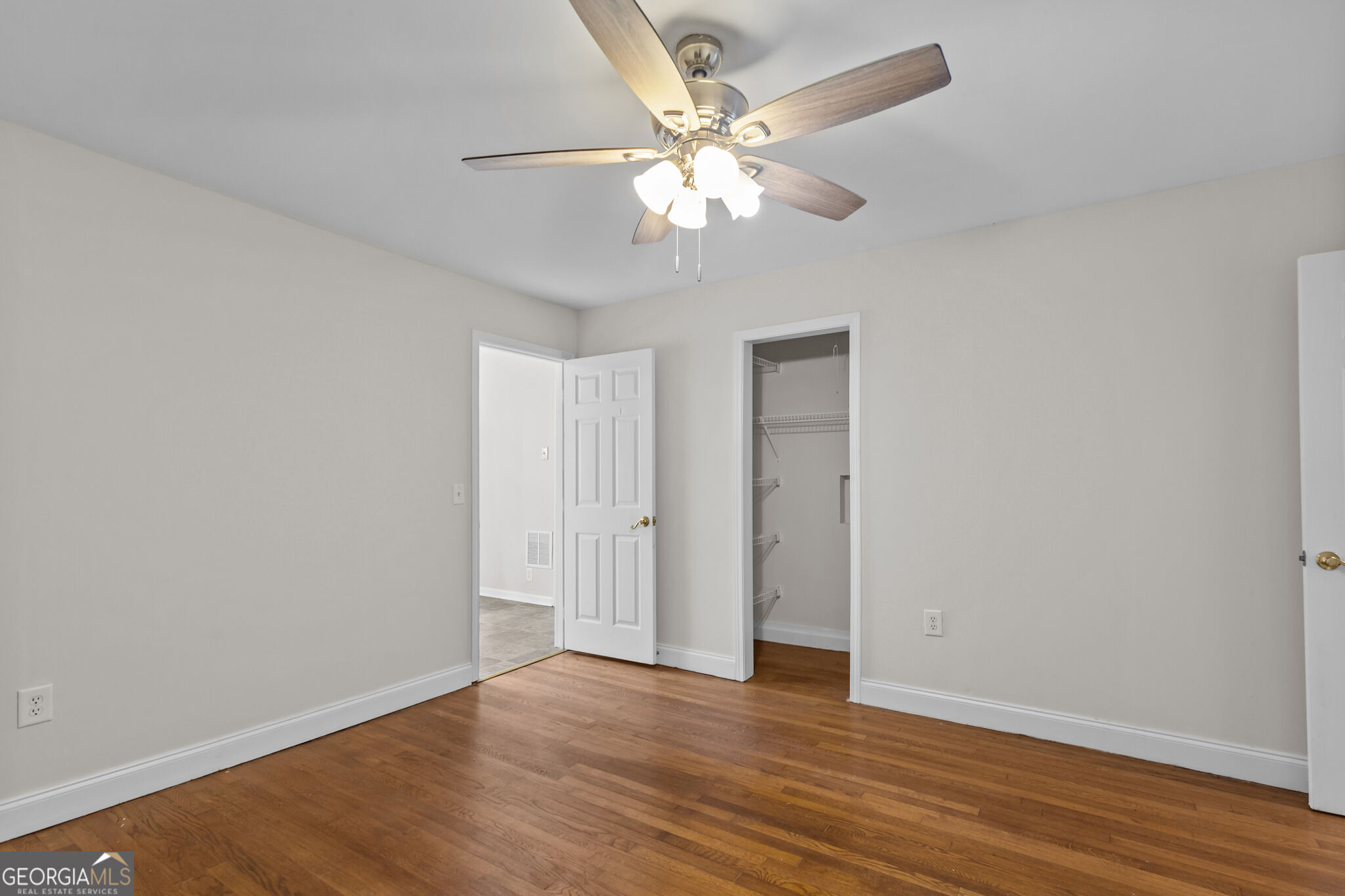 Empty bedroom with hardwood floors, ceiling fan, and an open closet with wire shelves.