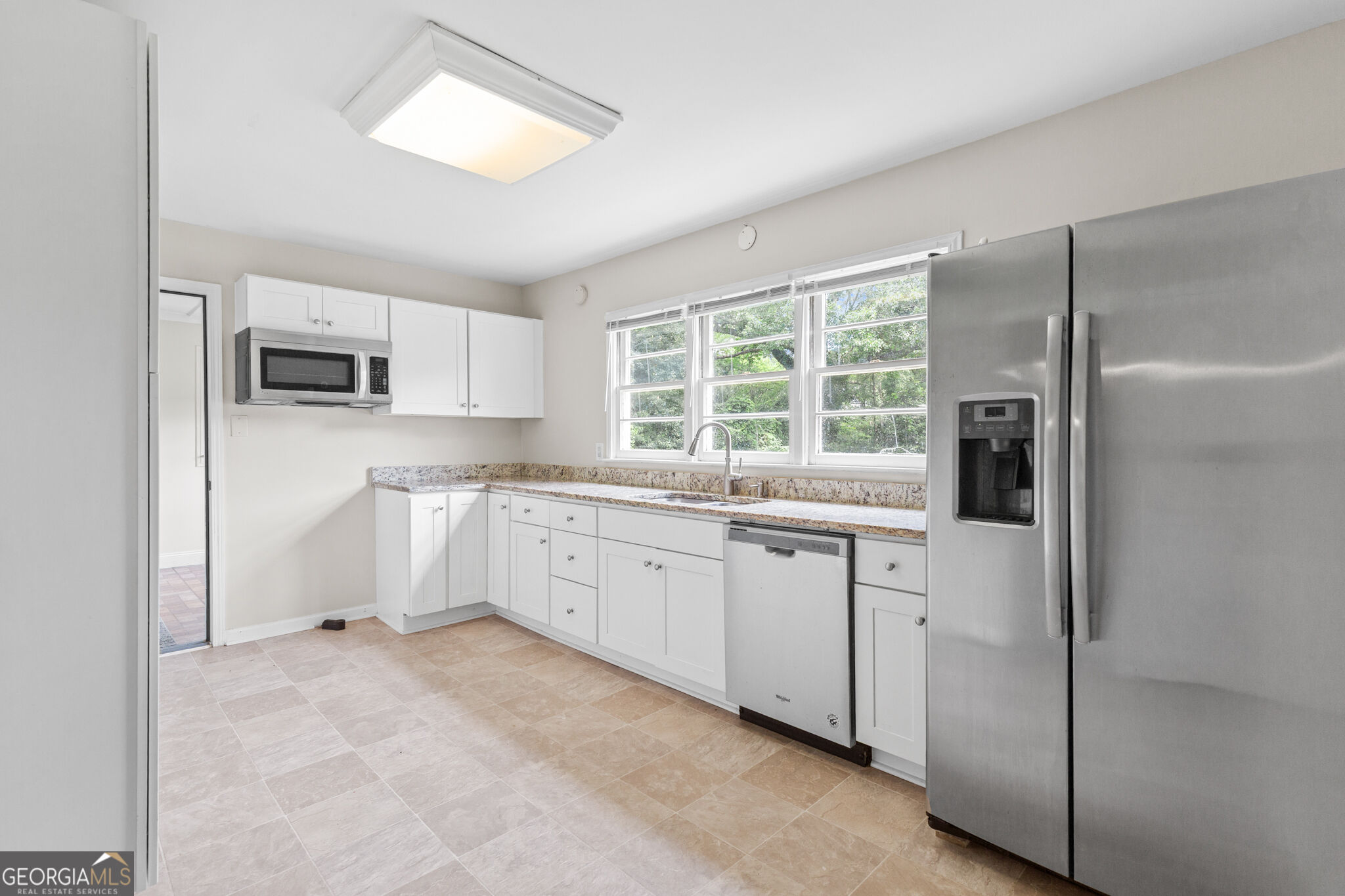 Kitchen with white cabinets, granite counters, stainless steel appliances, and three windows above the sink.