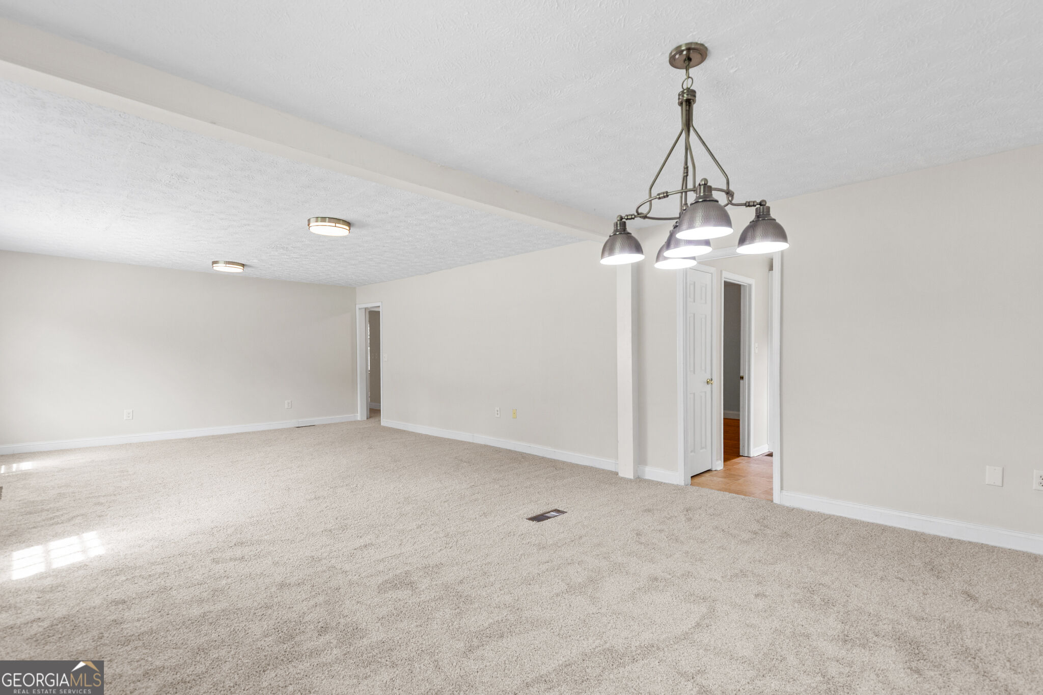 Spacious carpeted room with a multi-light pendant and open doorways.