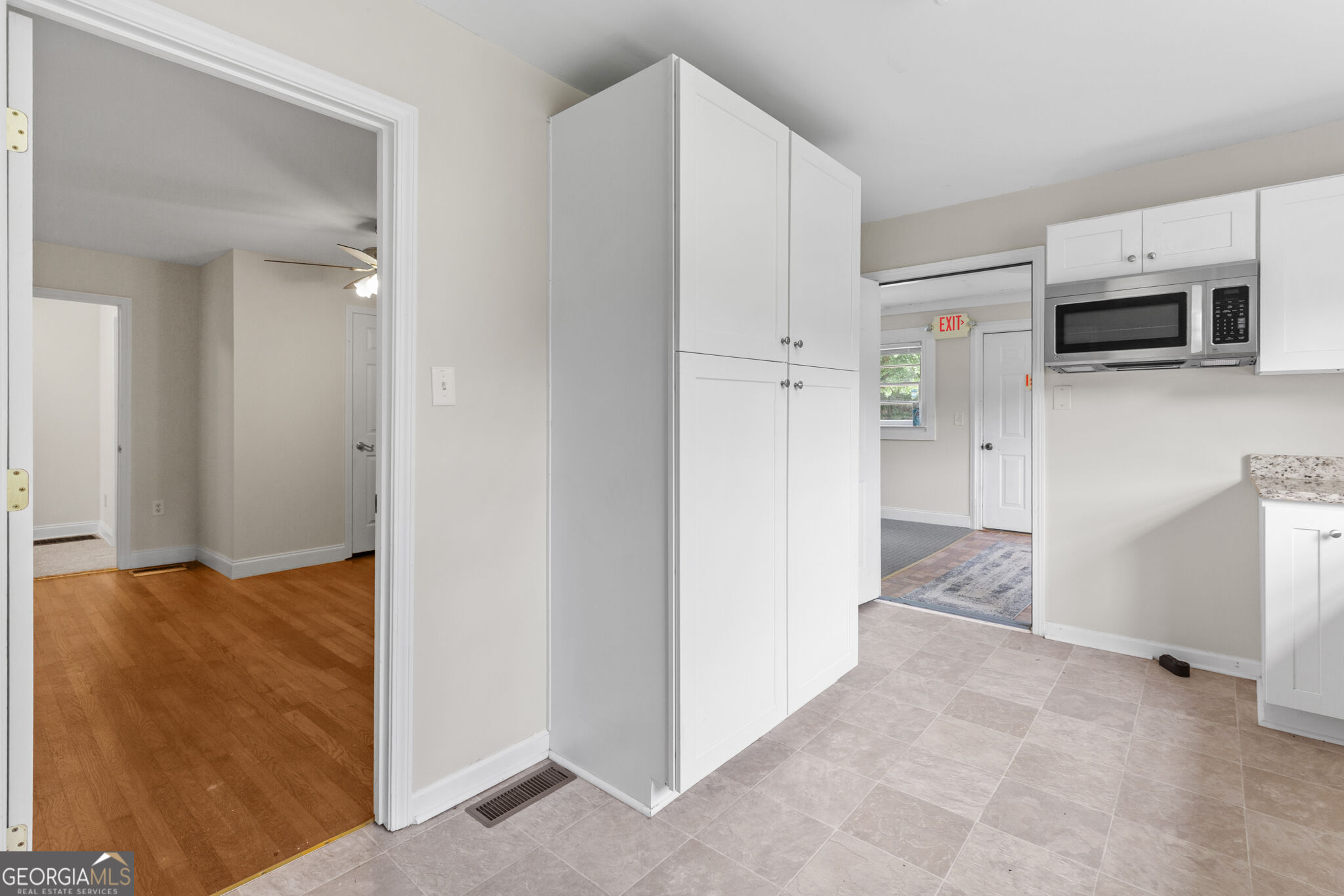 Kitchen with white cabinets and built-in microwave, opening to an adjoining room with hardwood floors.