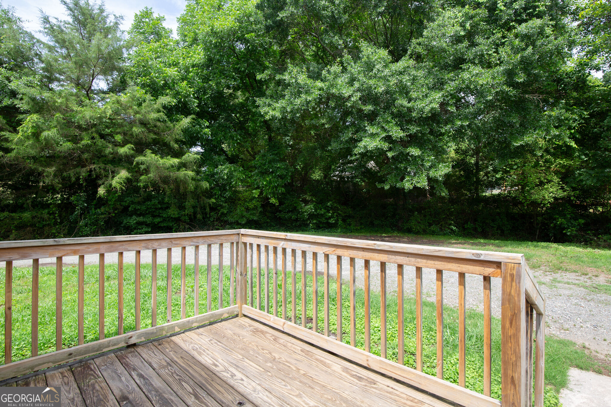Wooden deck with railings overlooking a grassy yard and dense trees.
