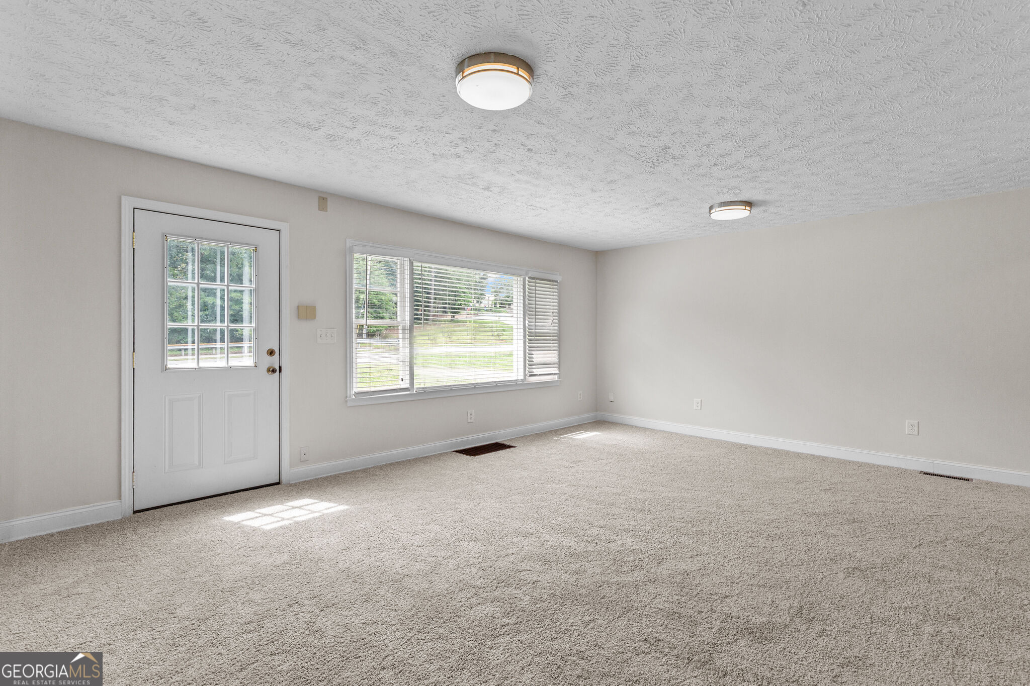 Empty carpeted room with a window and blinds beside a white exterior door.
