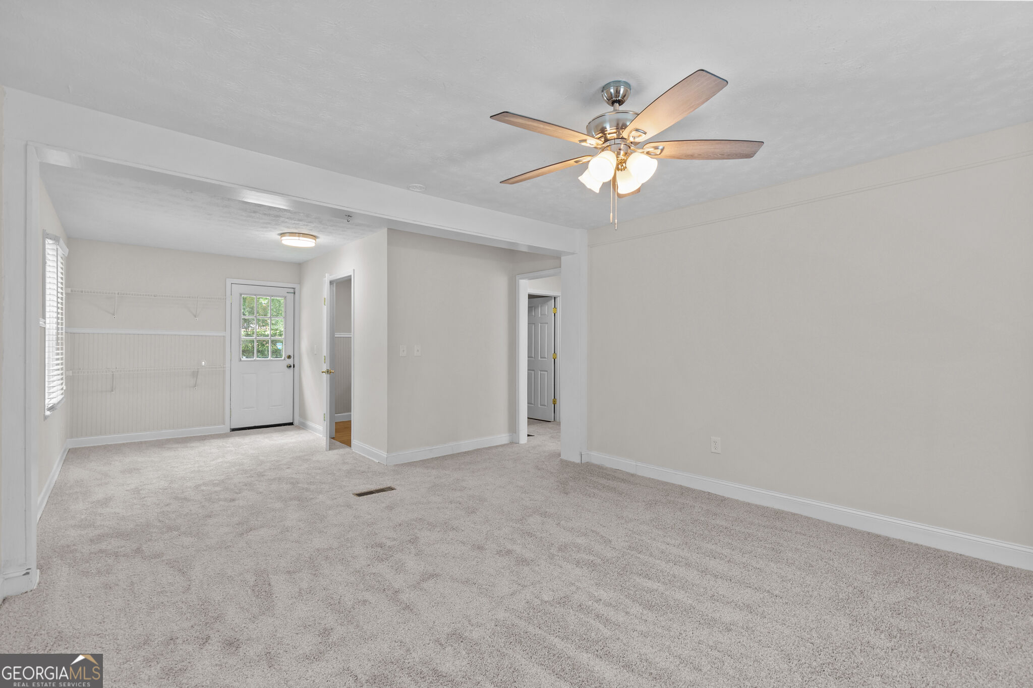Empty carpeted room with wainscoting, a window with blinds, and a ceiling fan.