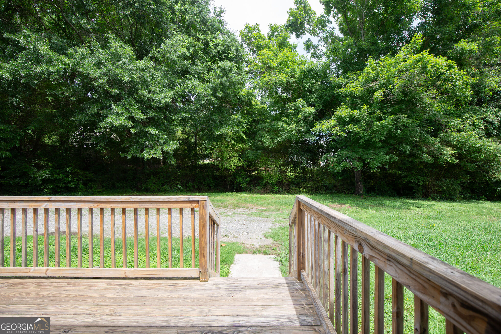 Wooden deck overlooking a grassy yard and dense wooded boundary.