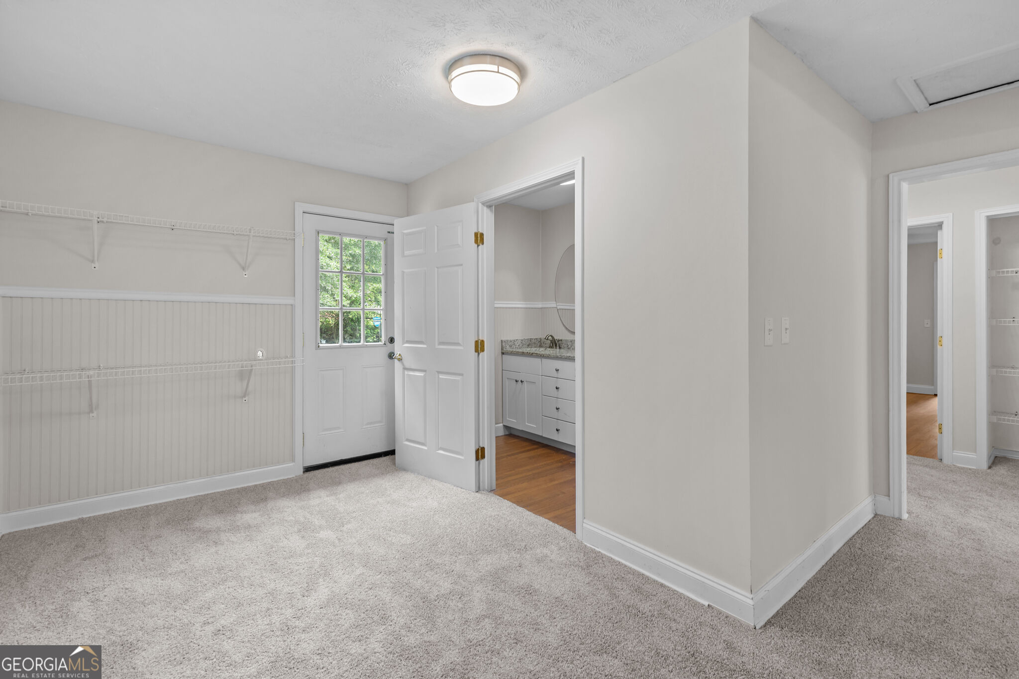 Carpeted room with wall shelving, a glass-paneled door, and an adjoining vanity area.