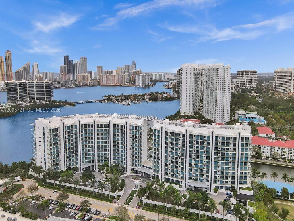 Waterfront condominium towers beside a bay, with boats and a distant city skyline.