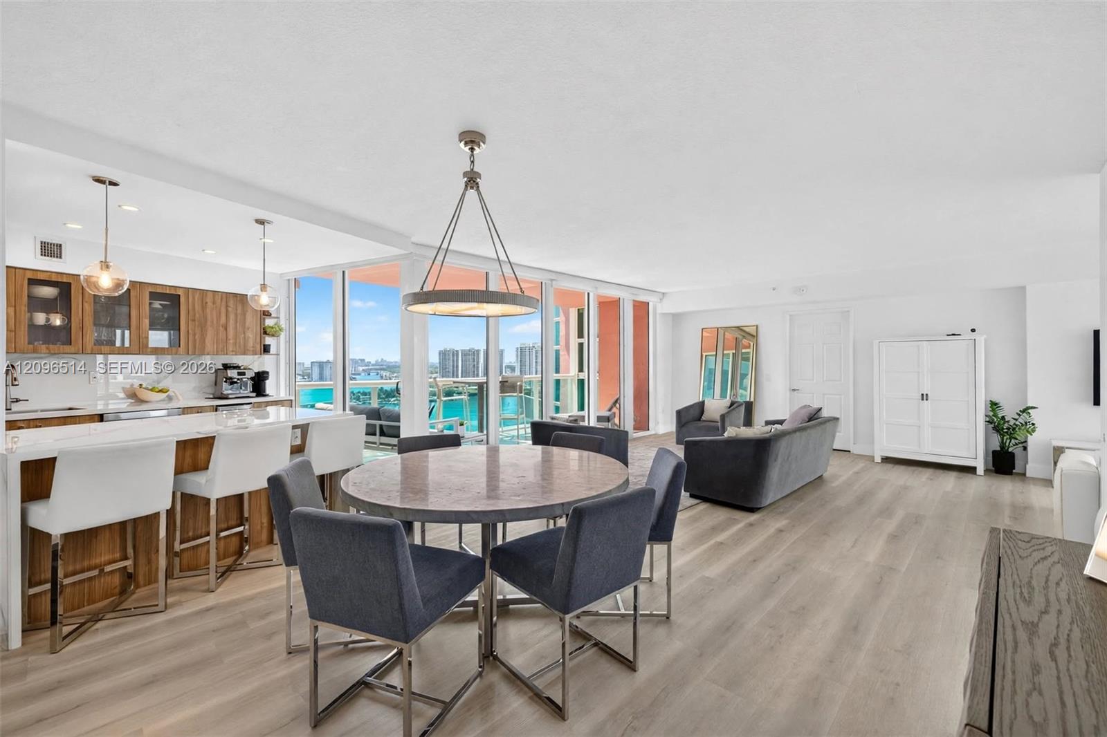 Open-plan condo with wood-accented kitchen, dining area, and turquoise water views through floor-to-ceiling windows.