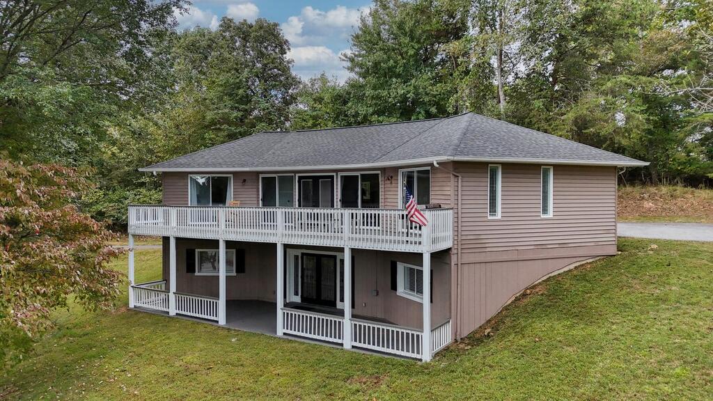 Raised home with a broad white deck and covered lower patio, surrounded by trees.