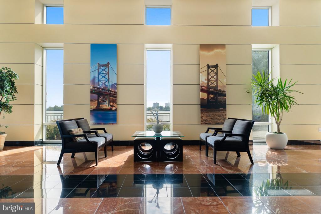 Furnished lobby seating area with polished stone floors, tall windows, and bridge artwork.