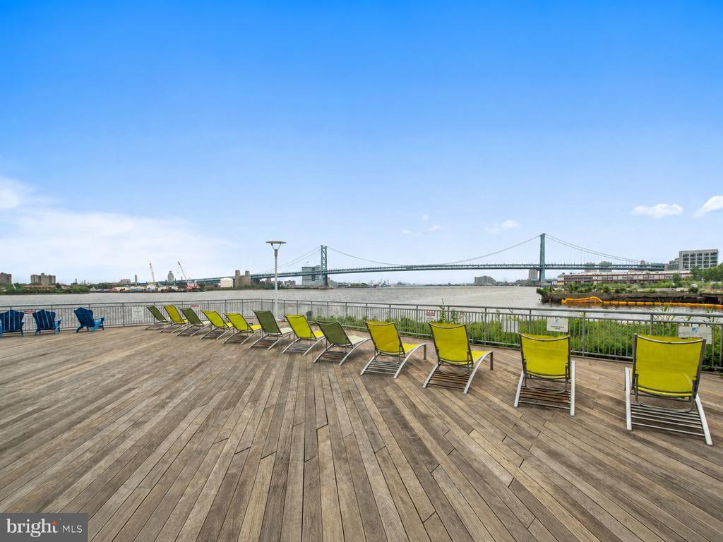 Riverside deck with yellow lounge chairs overlooking the Delaware River and Benjamin Franklin Bridge.