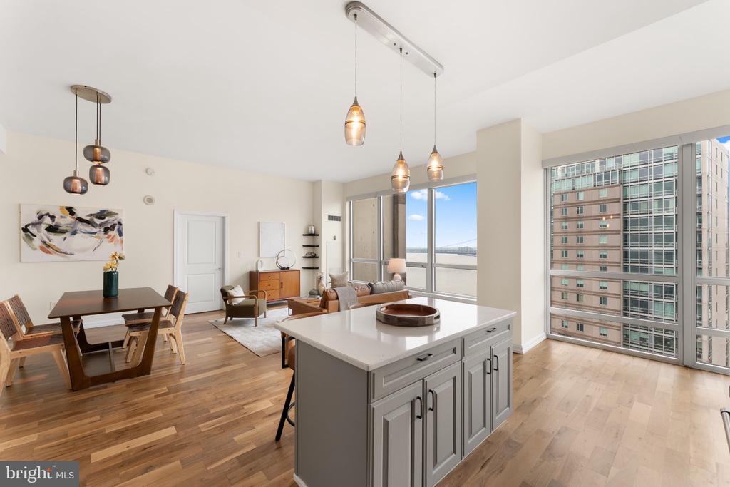 Open-plan condo kitchen and living area with a large island, hardwood floors, and floor-to-ceiling windows.