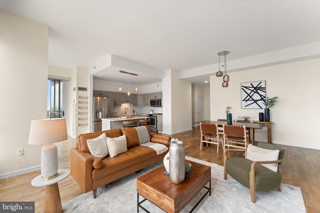Open-plan condo living room with a caramel leather sofa, wood coffee table, dining area, and adjoining gray kitchen.