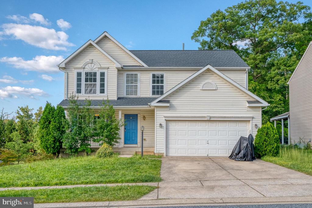 Two-story beige house with a blue front door, attached double garage, and driveway.