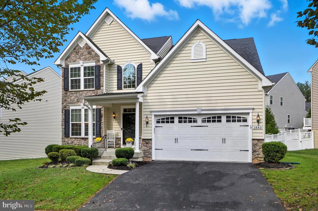 Two-story beige house with stone accents, dark shutters, and a double garage.