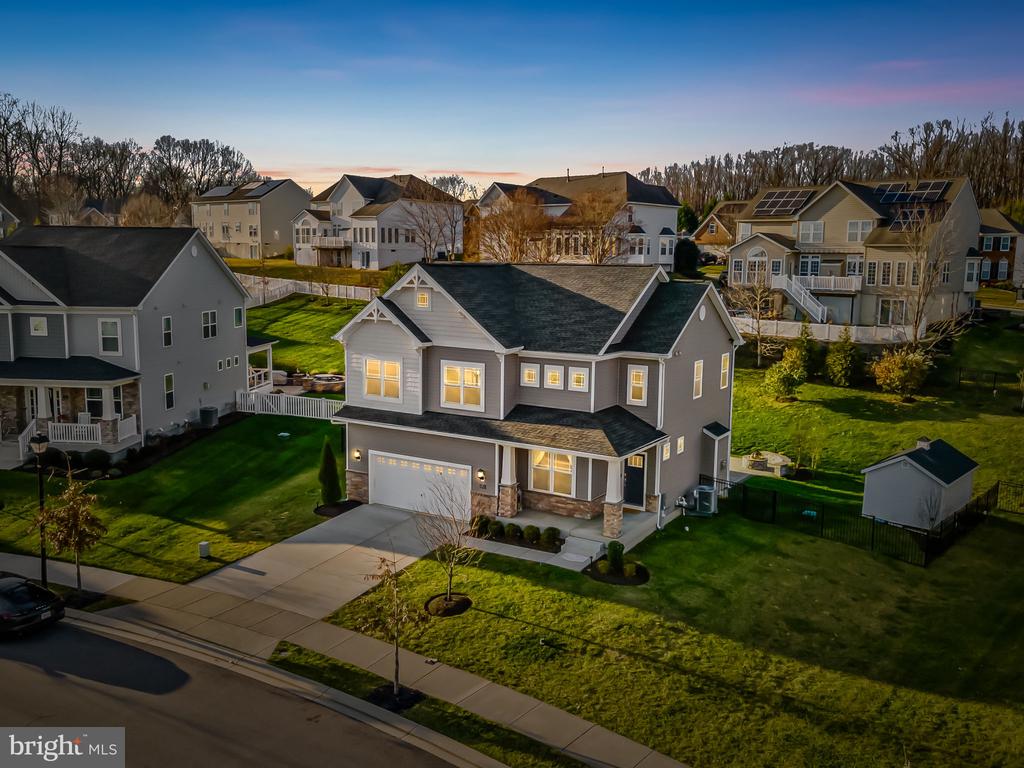 Aerial view of a two-story suburban home with lit windows and neighboring houses at dusk.