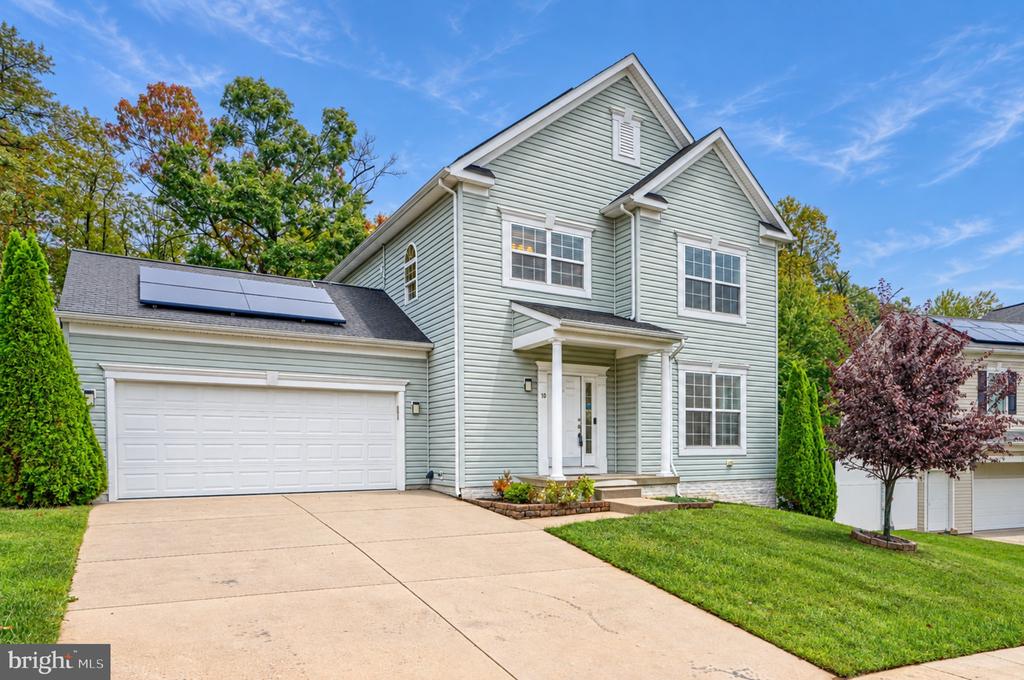 Pale green two-story house with a double garage, rooftop solar panels, and a wide driveway.