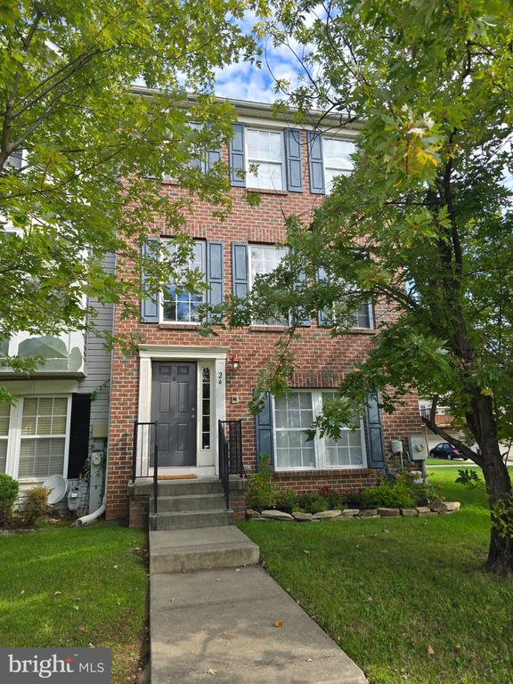 Brick townhouse with blue shutters, a front walkway, and mature trees in the foreground.