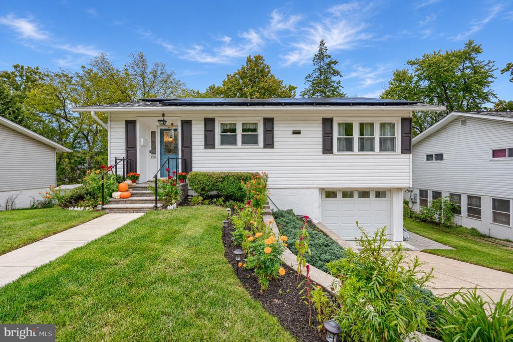 White split-level home with dark shutters, attached garage, and colorful front garden.