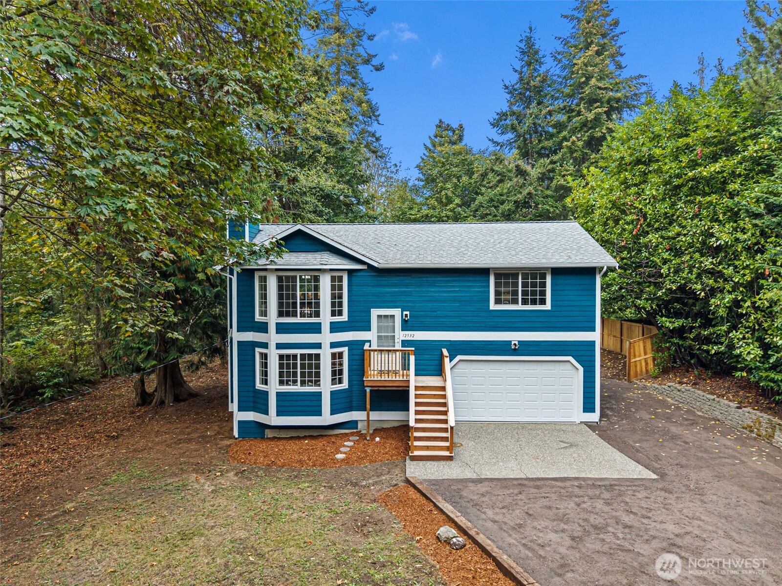 Blue two-story house with white trim, attached garage, and a wooded yard.
