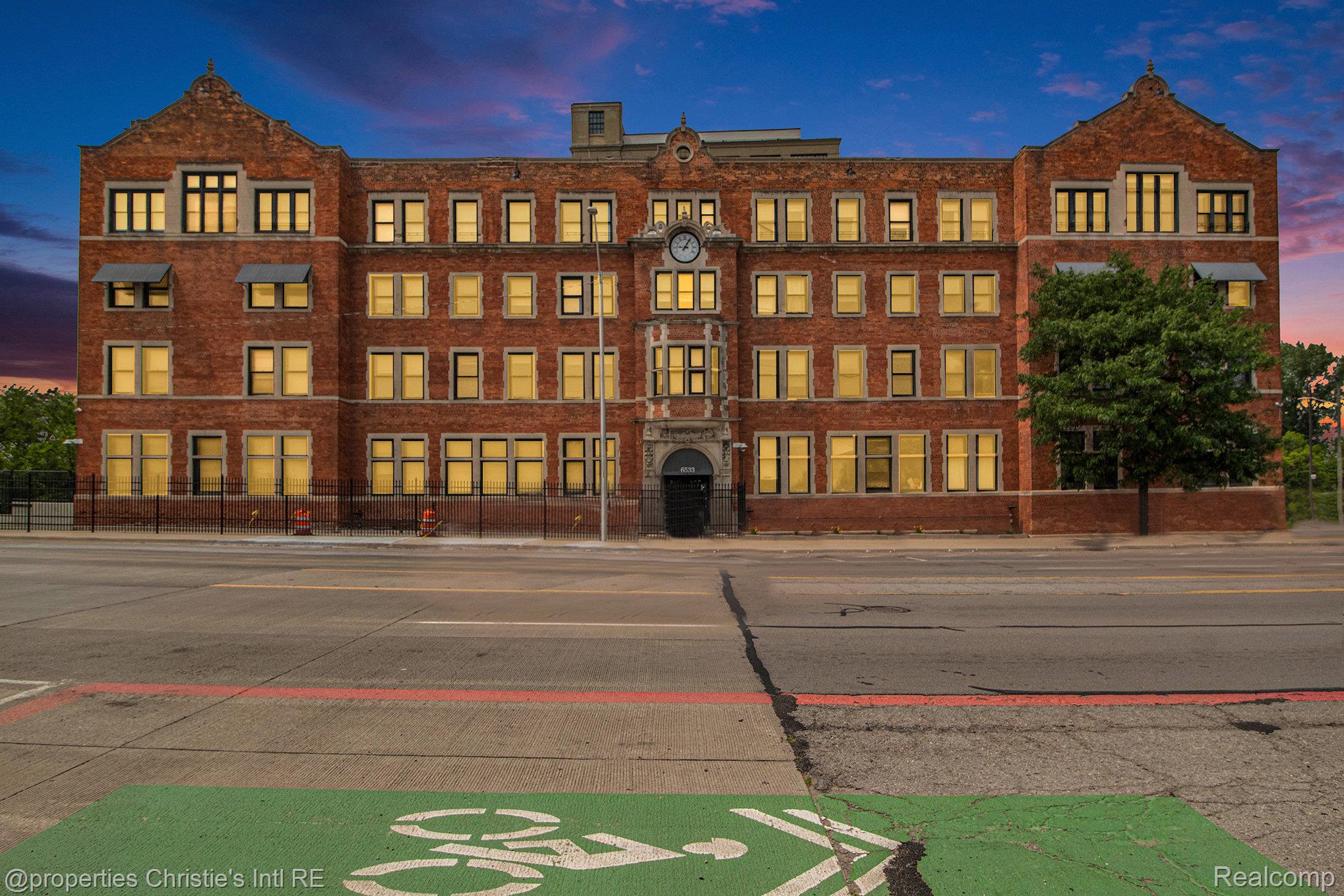 Red-brick building with a central clock and illuminated windows at dusk.