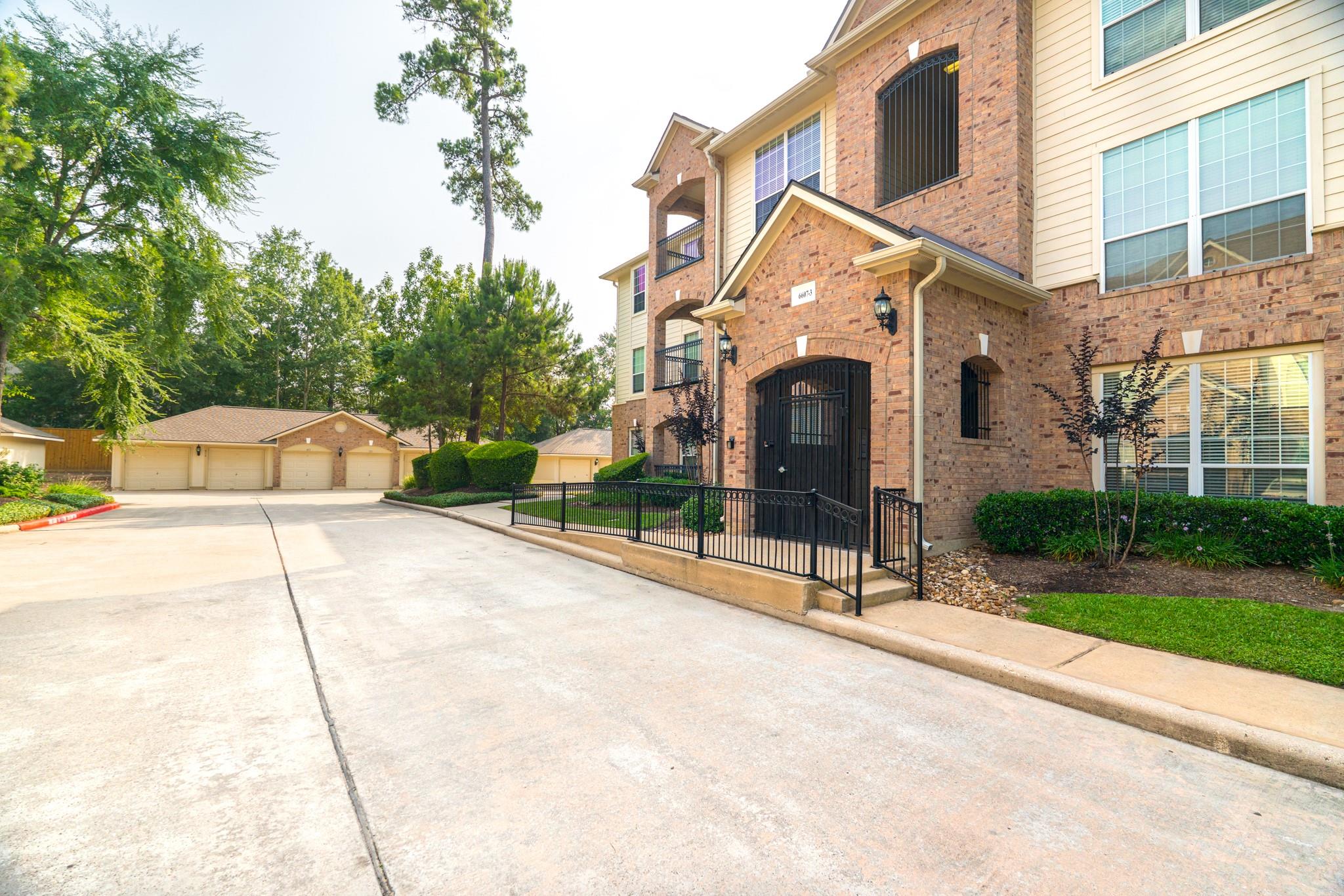 Brick multi-story residential building with balconies, a gated entrance, and detached garages beside it.
