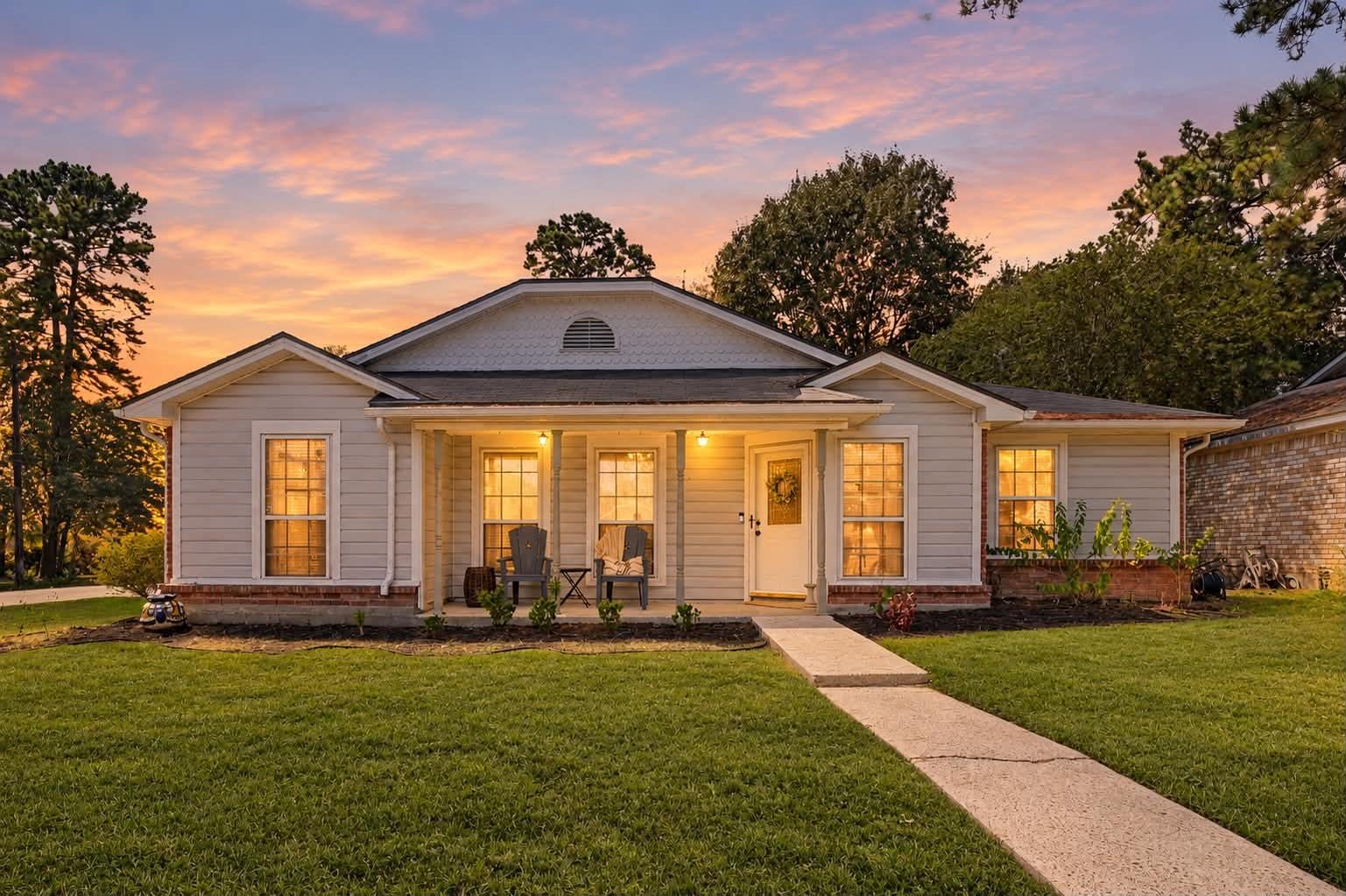 Single-story gray house with a covered porch and glowing windows at sunset.