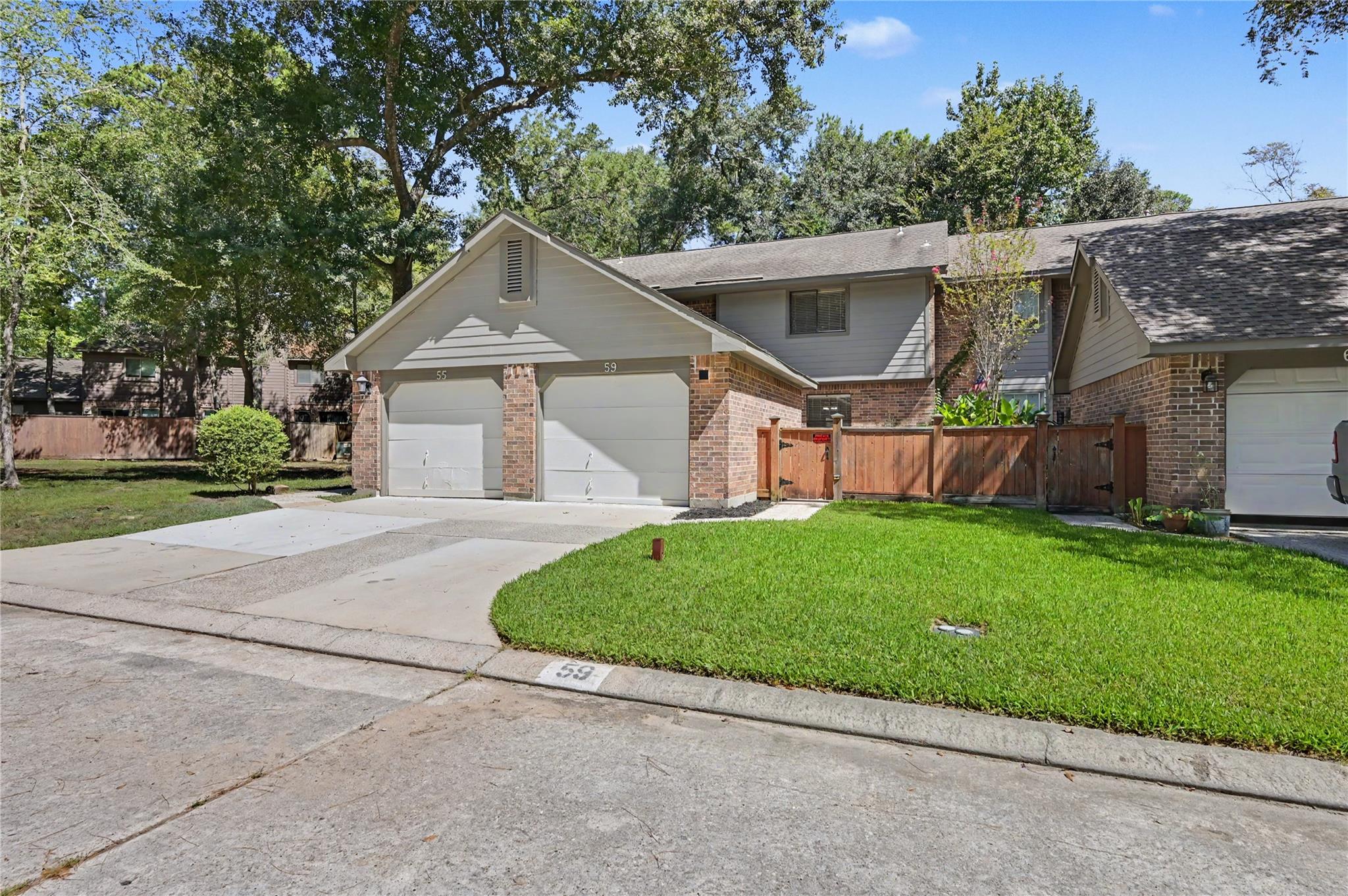 Attached brick homes with numbered garages, a fenced lawn, and mature shade trees.