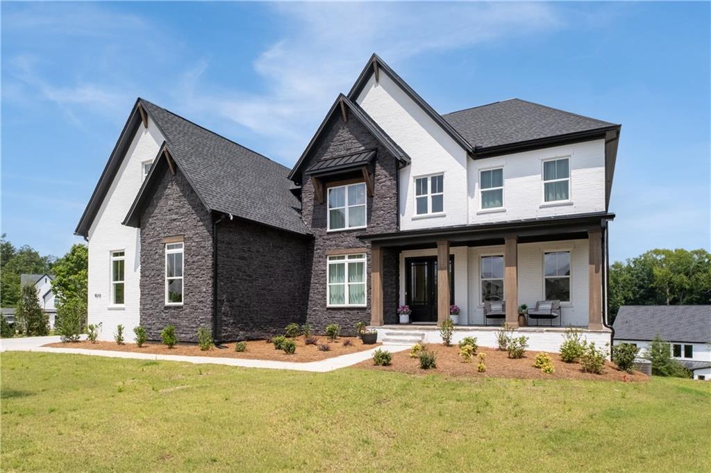 Two-story white brick and dark stone house with a covered porch and broad lawn.
