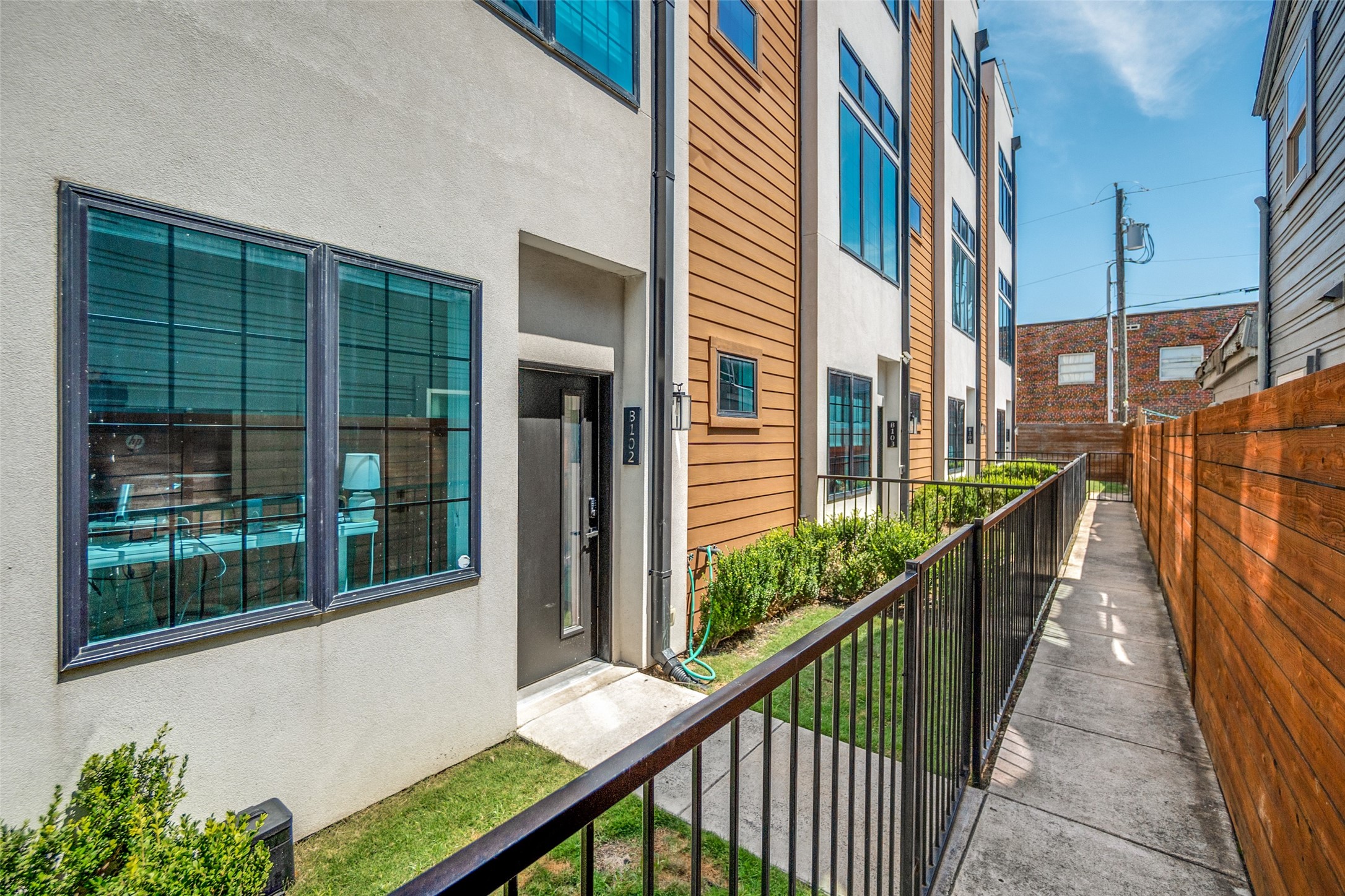 B102 entrance along a fenced walkway beside a modern residential building.