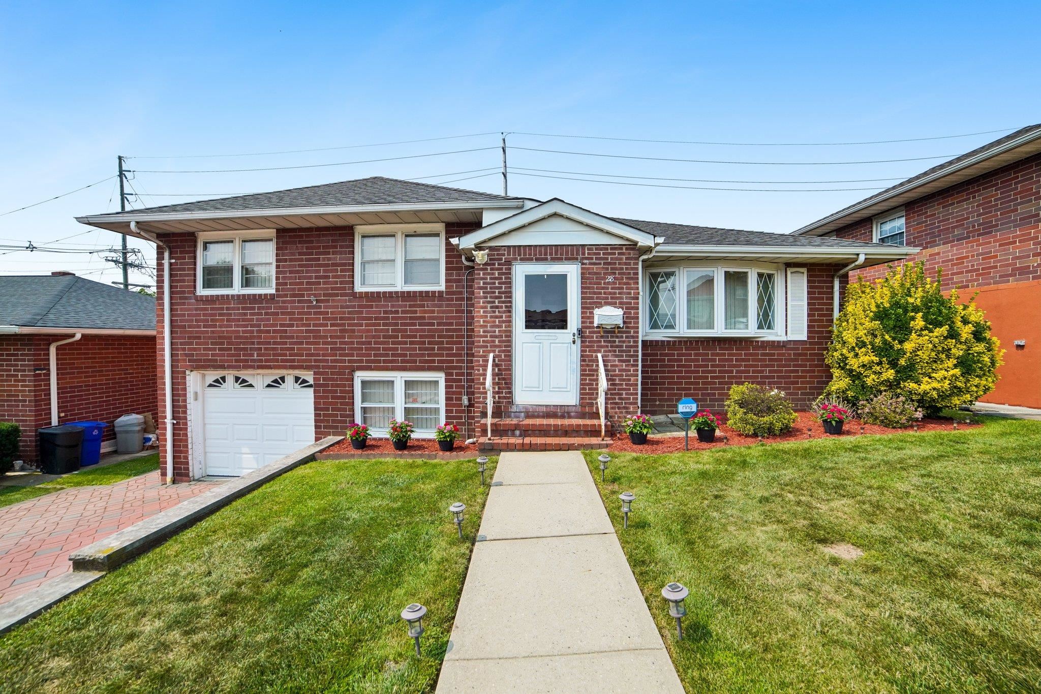 Red-brick split-level house with a white front door, garage, and landscaped front lawn.